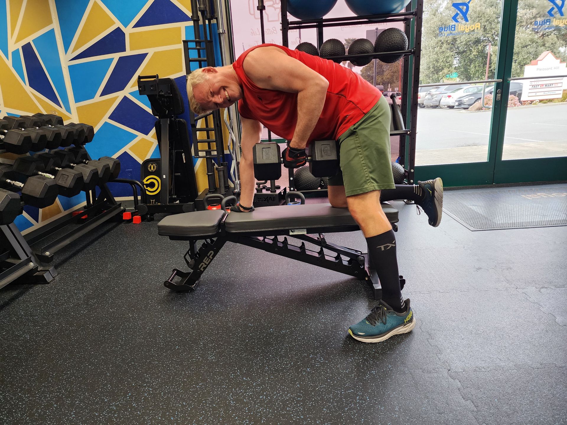 Man in red shirt performing a dumbbell row for strength training with a pleasant smile on his face in a well equipped gym