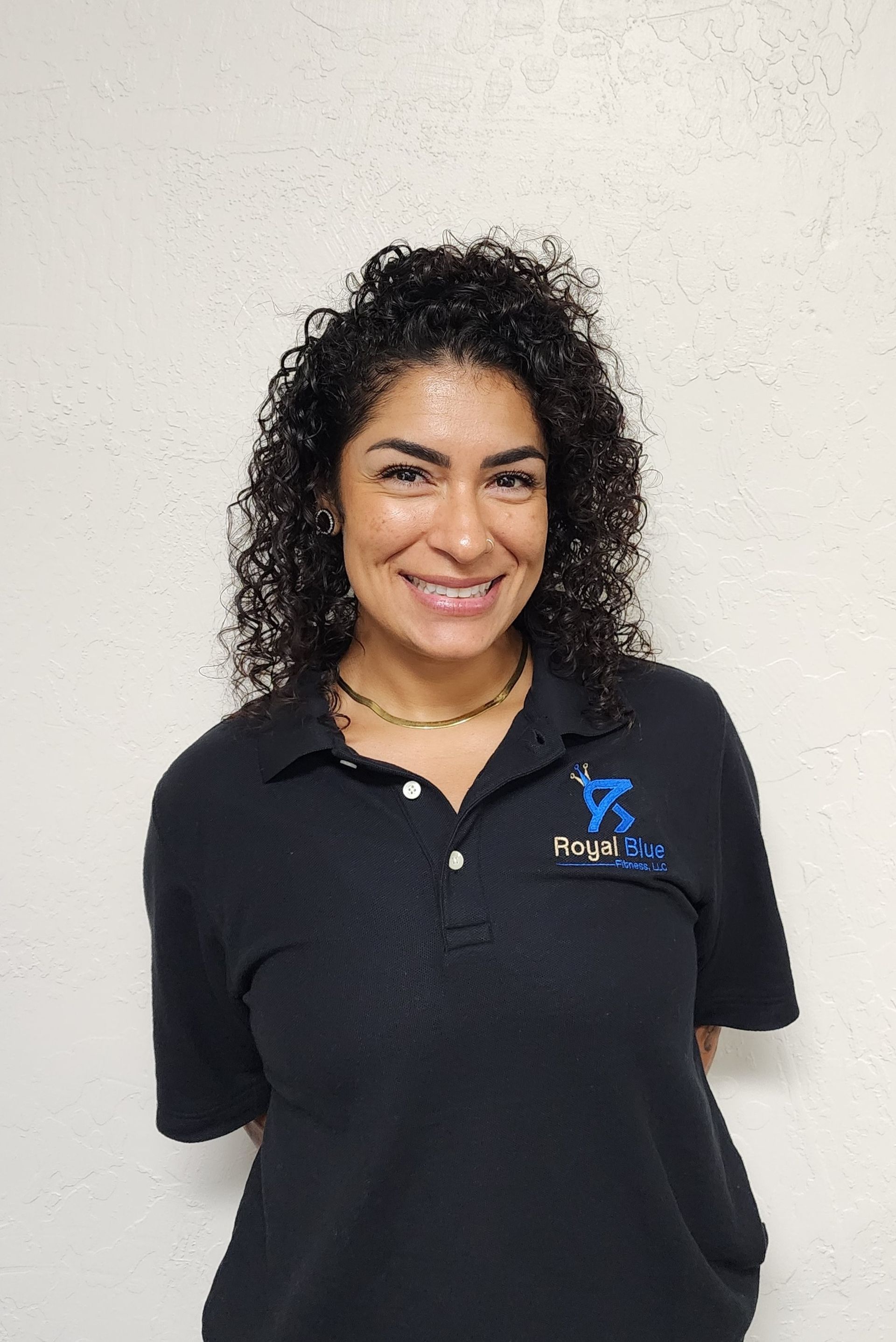 Kennedy Rizon in a black polo shirt with the Royal Blue Fitness logo, standing confidently with arms crossed.