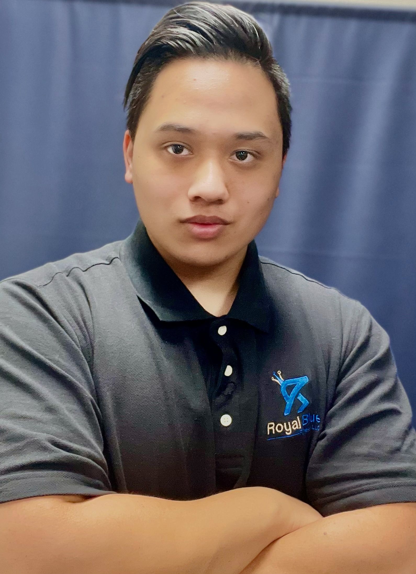 Kennedy Rizon in a black polo shirt with the Royal Blue Fitness logo, standing confidently with arms crossed.