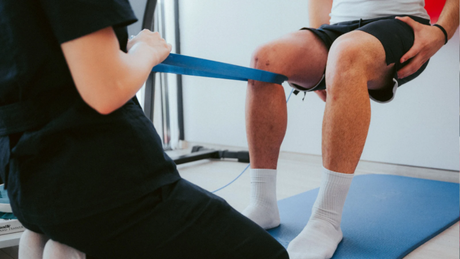 Prehab & post-injury training guided by our structured system. Coach guiding knee rehabilitation with a resistance band as the client performs controlled movement on a blue mat.