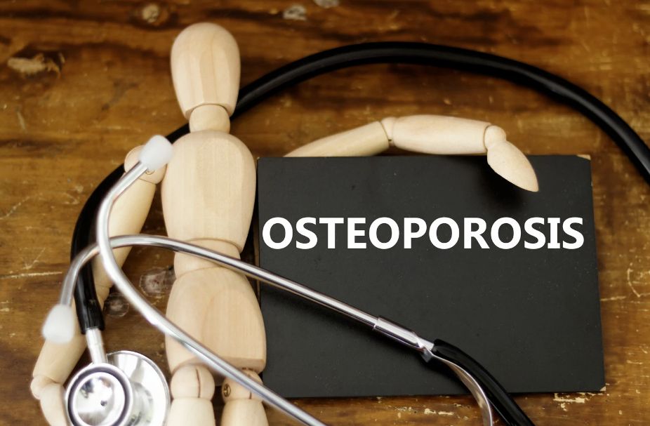 Wooden mannequin with a stethoscope next to a black card reading 'OSTEOPOROSIS' on a wooden table, representing a medical concept.