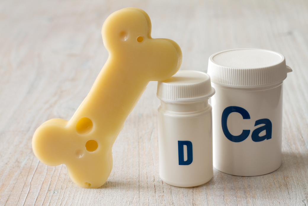 A bone-shaped model with holes demonstrating osteoporosis, next to supplement bottles labeled 'D' for vitamin D and 'Ca' for calcium.