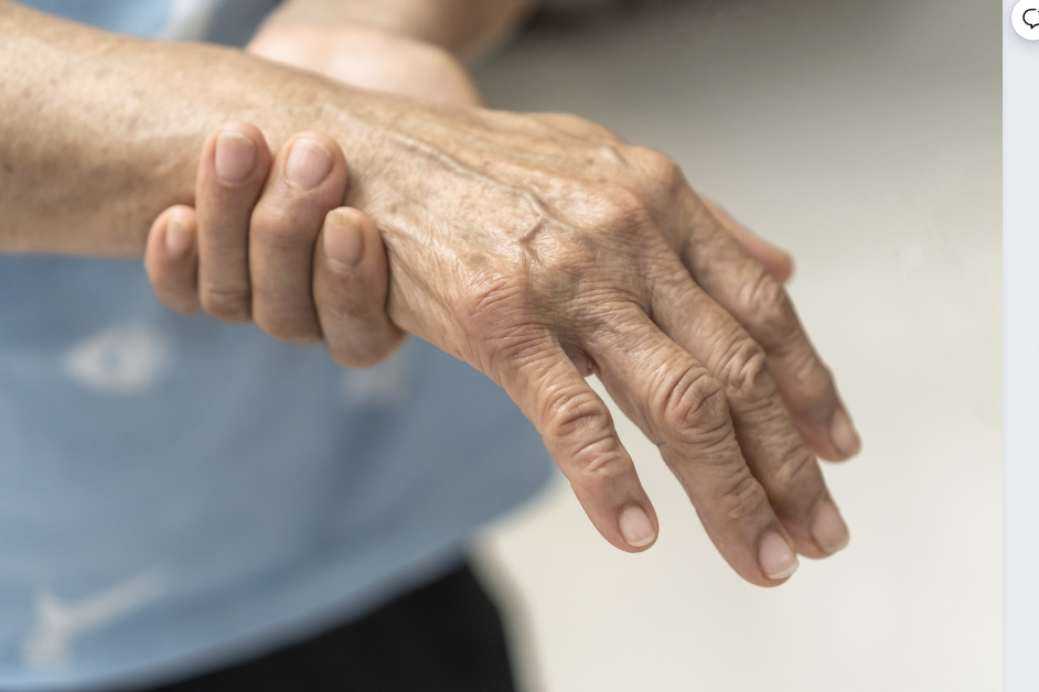 An older adult's hands showing signs of arthritis, with one hand supporting the other in a gentle grasp.