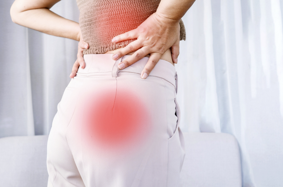 A person stands with a hand on the lower back, indicating sciatic pain highlighted by a red glow over the affected area.