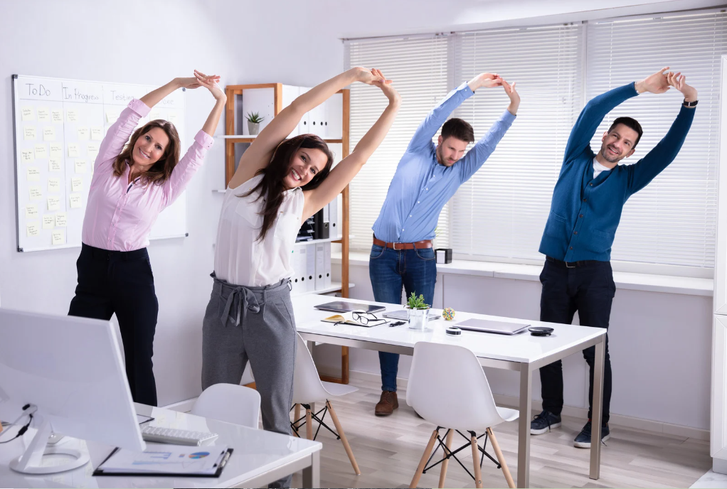  Four office workers stretch together to improve posture, smiling by their desks