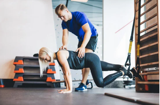 A personal trainer in a blue shirt attentively guiding a senior client through a barbell exercise with proper form for safety