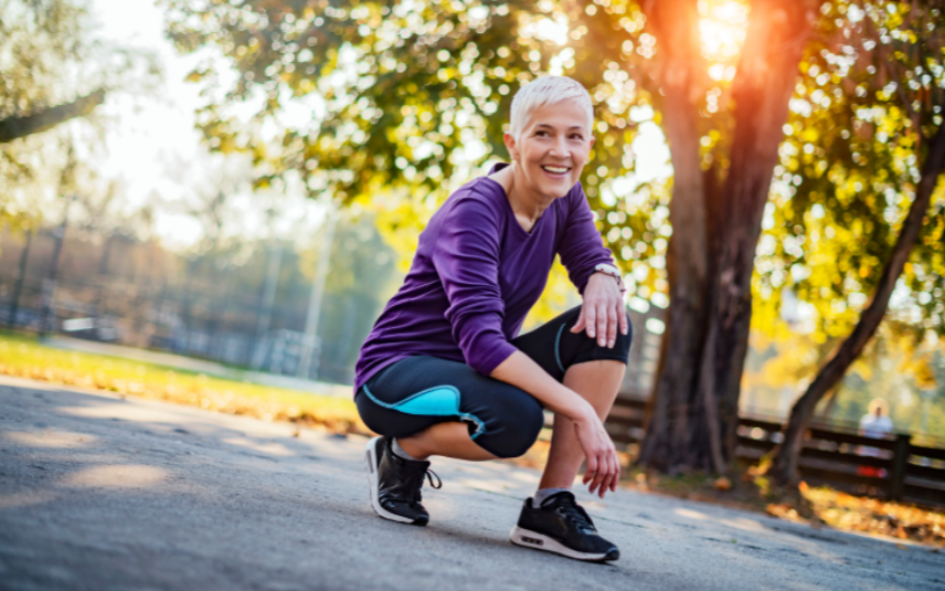 Strong for Life: health-smart training for energy, bone strength, and healthy aging. Smiling active woman in athletic wear kneeling in a sunny park after a workout.