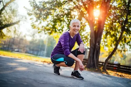 Strong for Life: health-smart training for energy, bone strength, and healthy aging. Smiling active woman in athletic wear kneeling in a sunny park after a workout.