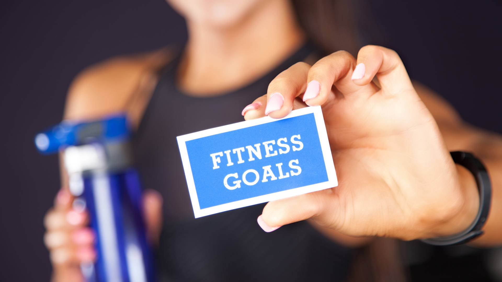 A woman holding a card that reads “Fitness Goals,” representing goal setting and sustainable fitness
