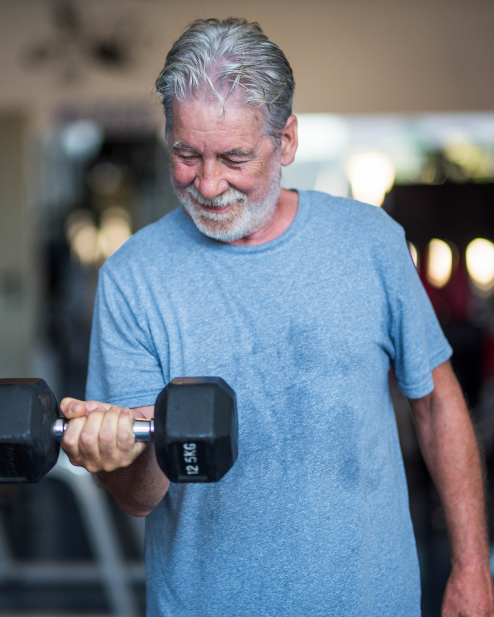 Mature adult man performing a dumbbell curl in a gym, smiling during strength training.