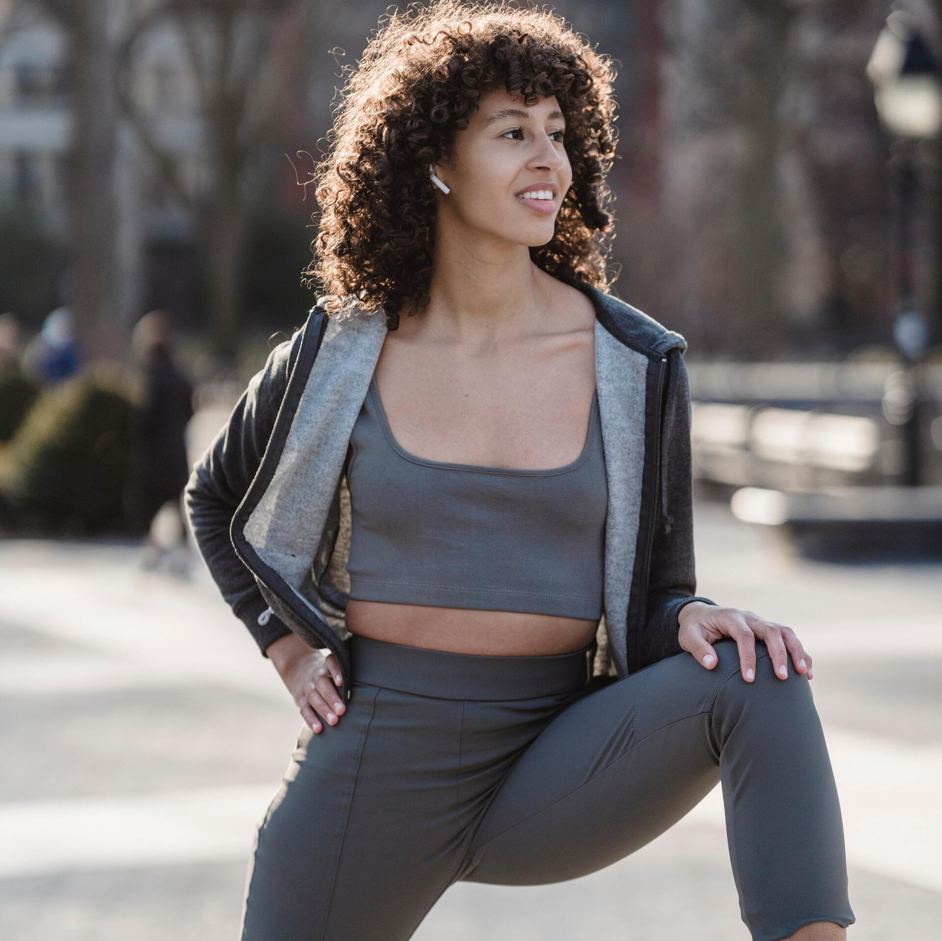 A woman in a grey gym outfit performing a hip flexor stretch, focusing on flexibility and mobility in the hip area.