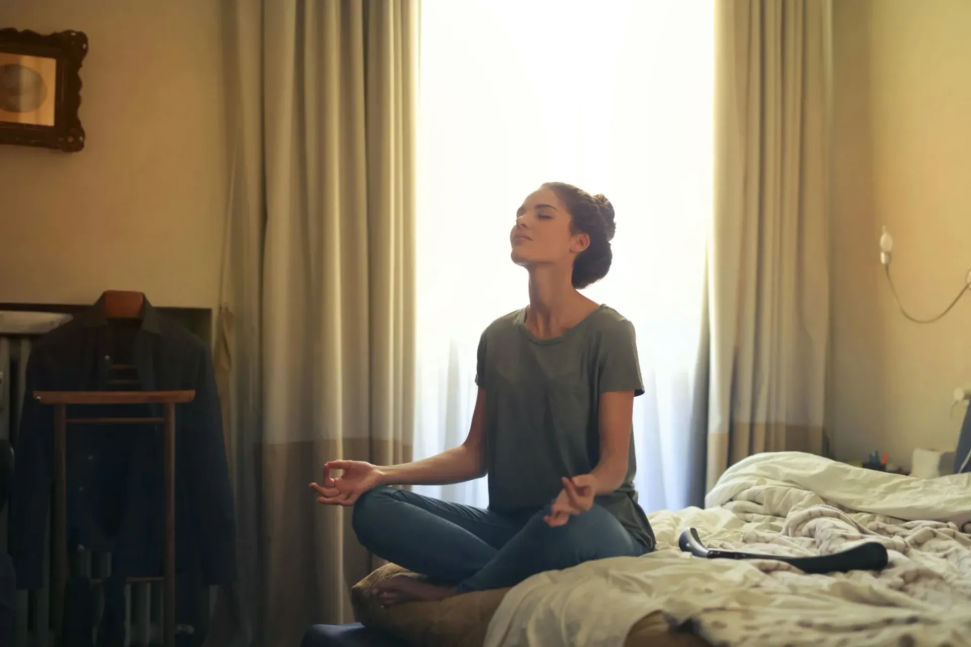A woman sits cross-legged on a bed, practicing breathing and relaxation as part of herstress relief.