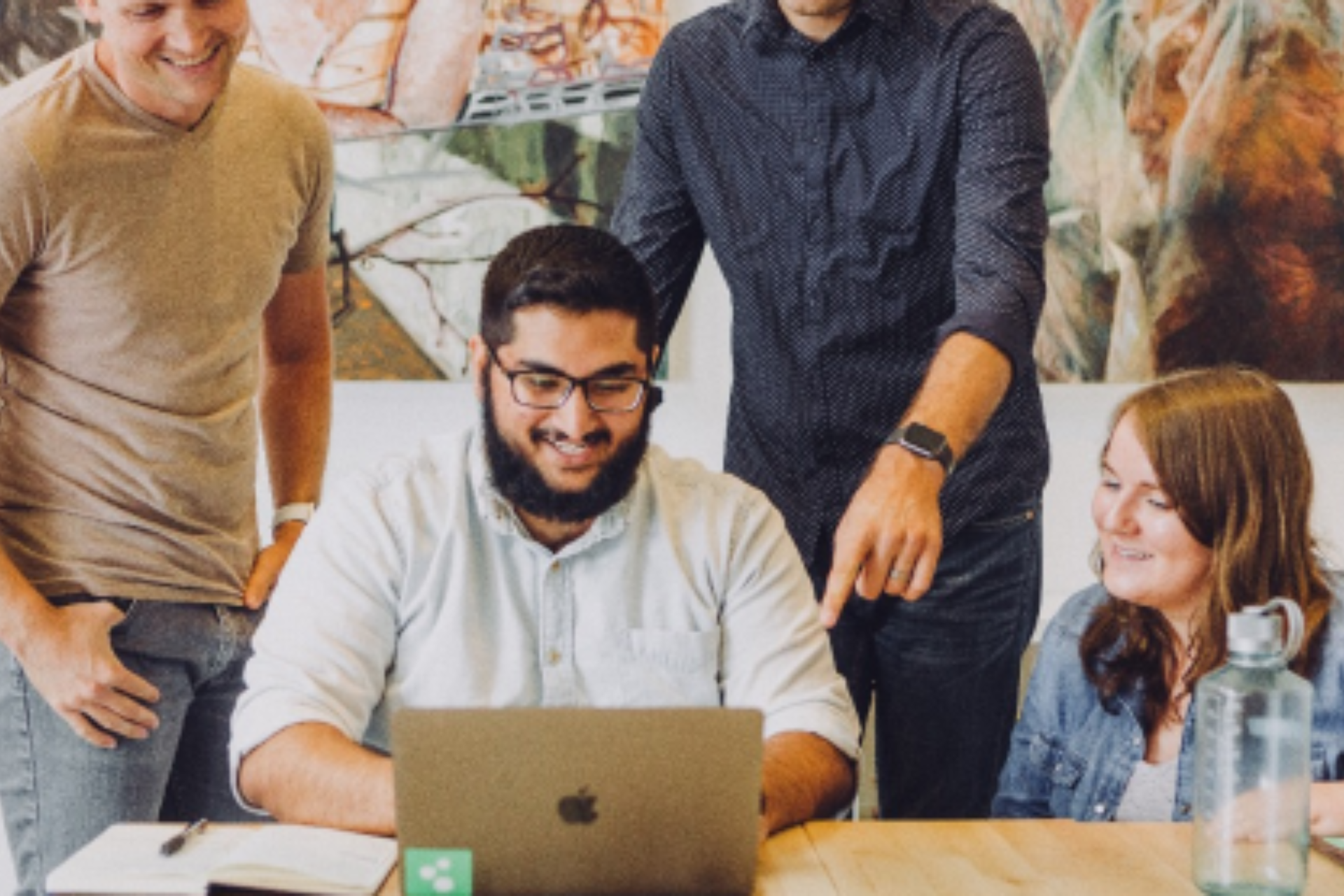 A group of people are standing around a table looking at a laptop computer.