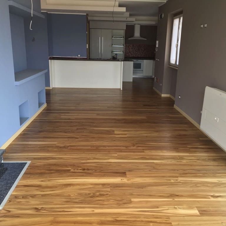 Una stanza vuota con un pavimento in legno e una cucina sullo sfondo