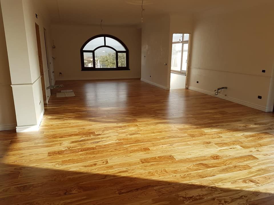 Una grande stanza vuota con un pavimento in legno e una finestra.