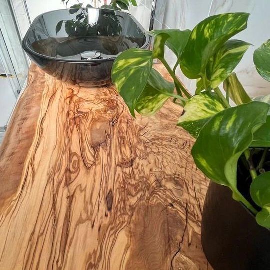 Una pianta in vaso è appoggiata su un tavolo di legno accanto a un lavandino.
