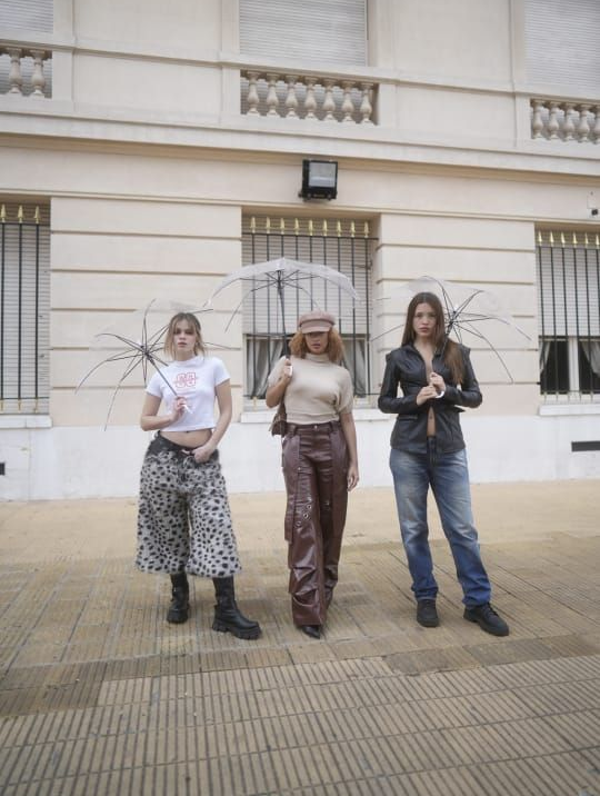 Tres personas con paraguas transparentes posan frente a un edificio.