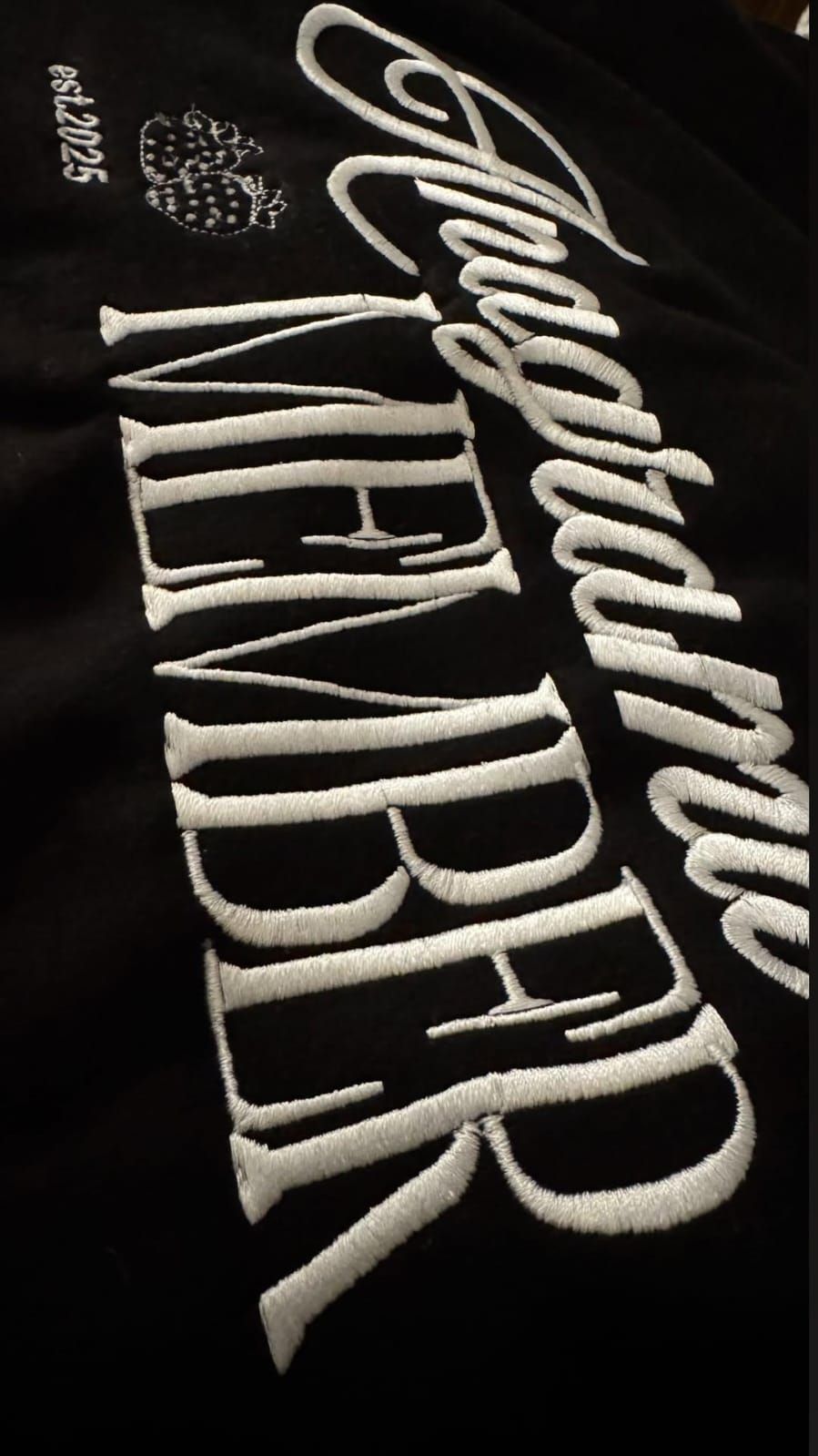 Persona con sudadera negra con capucha y letras, sentada en un banco de madera, mirando al agua. Se ve un salvavidas.