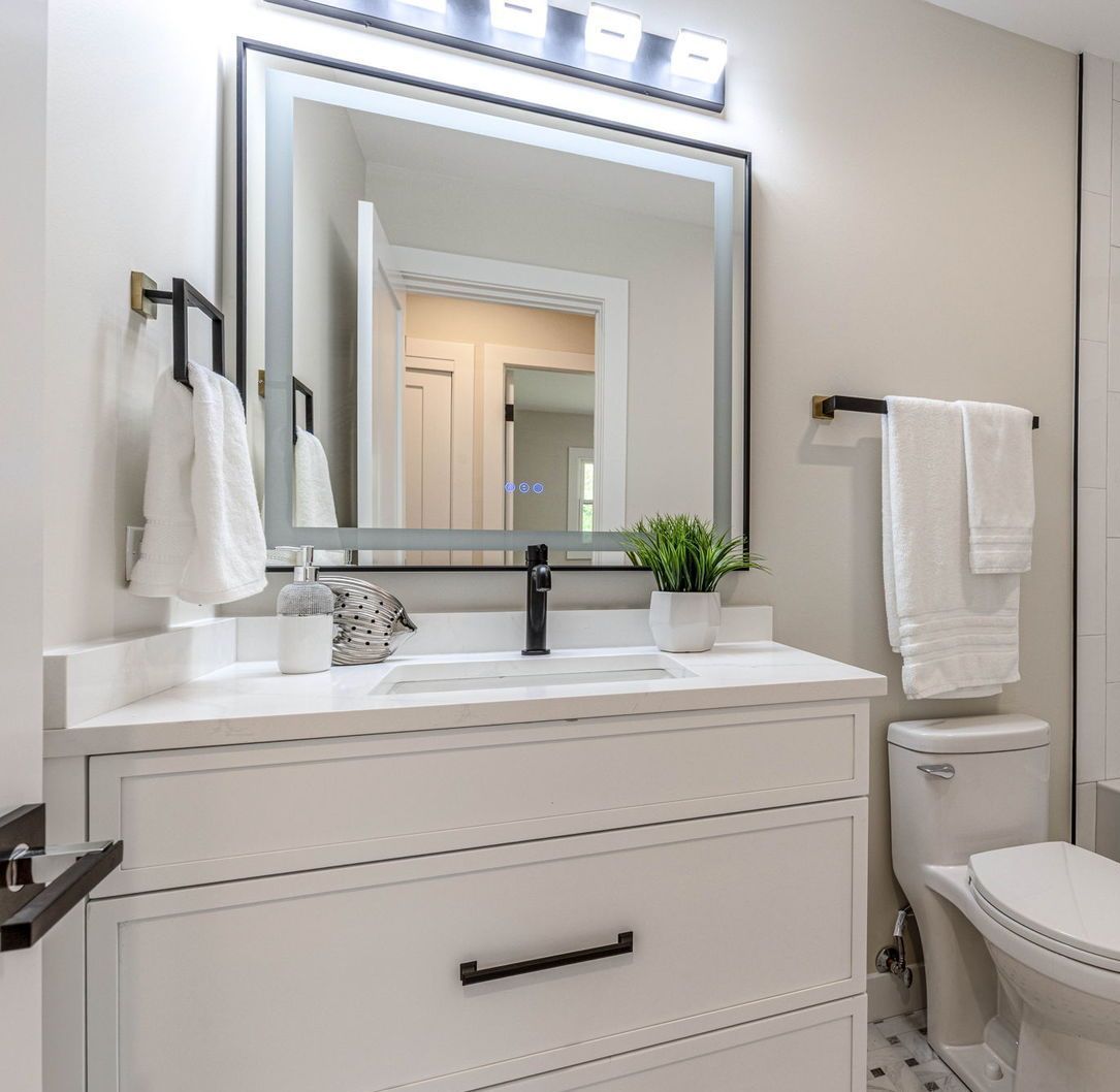 White bathroom with vanity, mirror, and toilet; black accents.