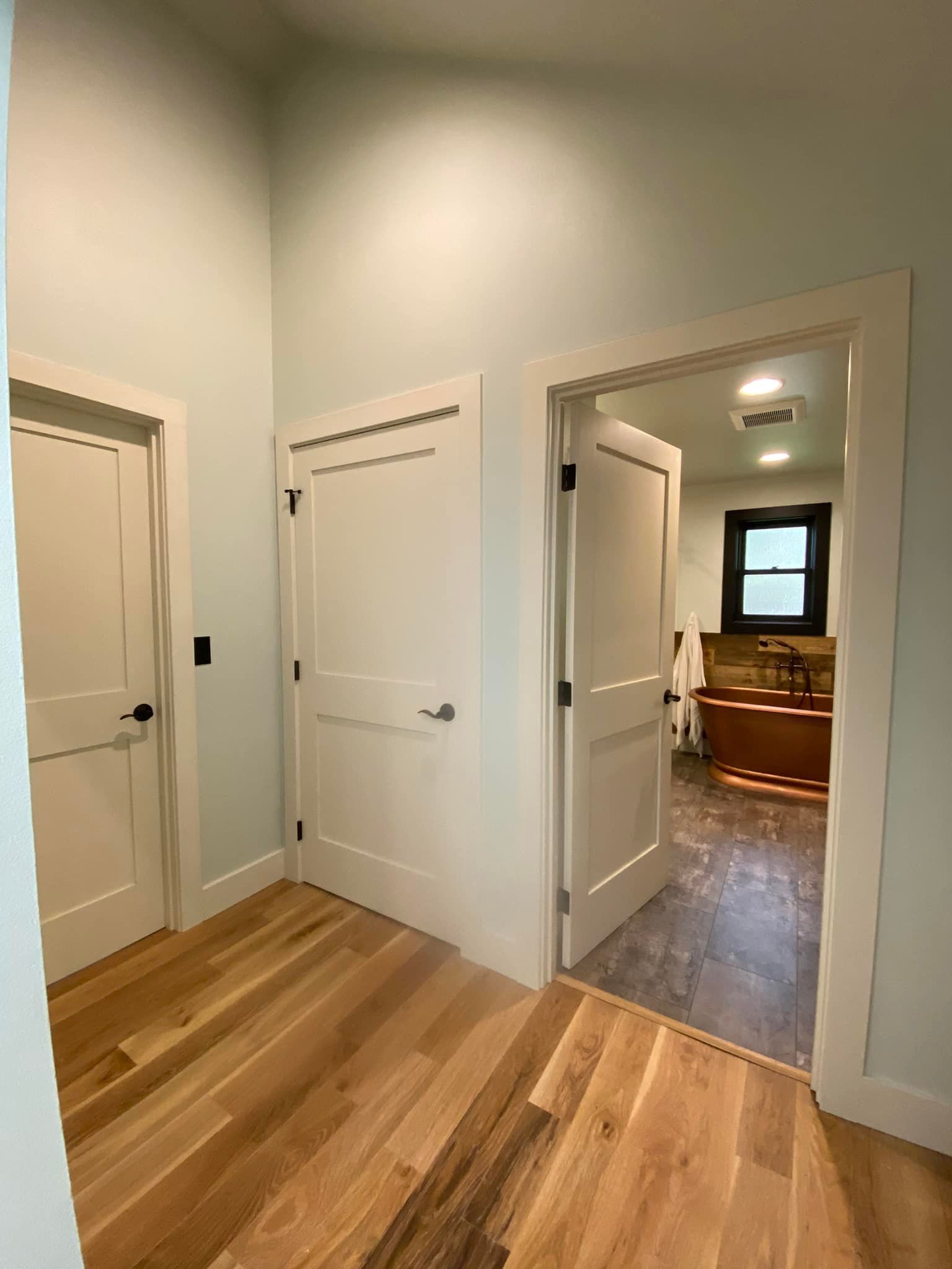 A hallway with hardwood floors and white doors leading to a bathroom.
