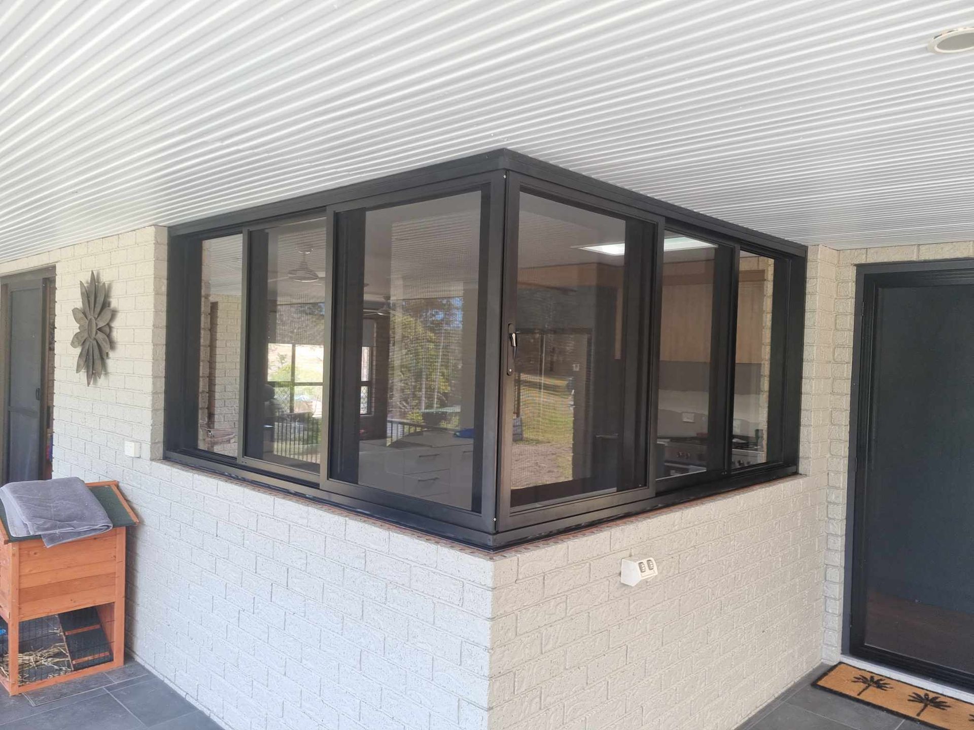 Corner windows in black frames set into a white brick wall, under a corrugated ceiling — K & J Glass in Scotts Head, NSW
