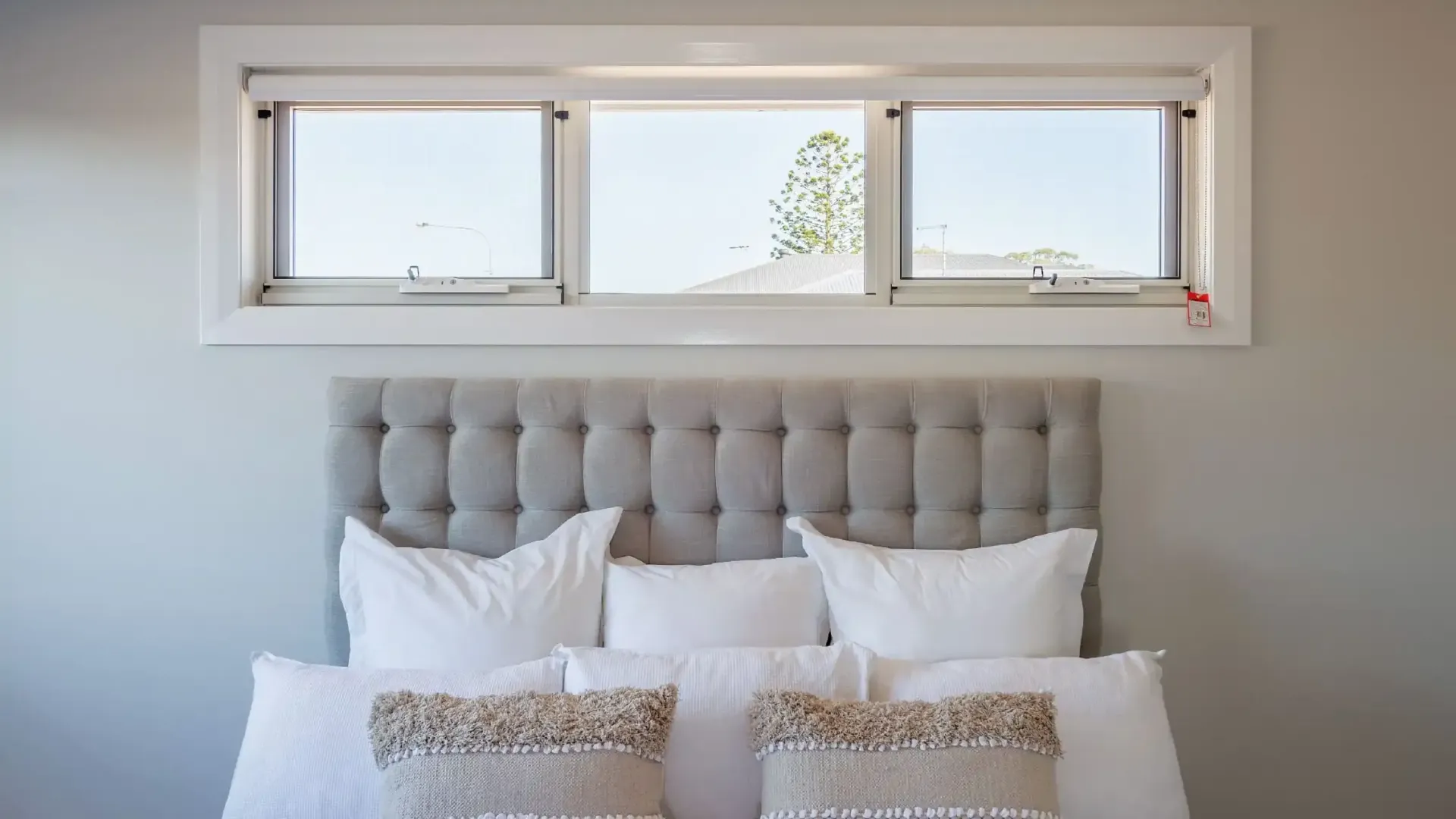 Bedroom with gray tufted headboard, white pillows, and three-panel window above — K & J Glass in Warrell Creek, NSW