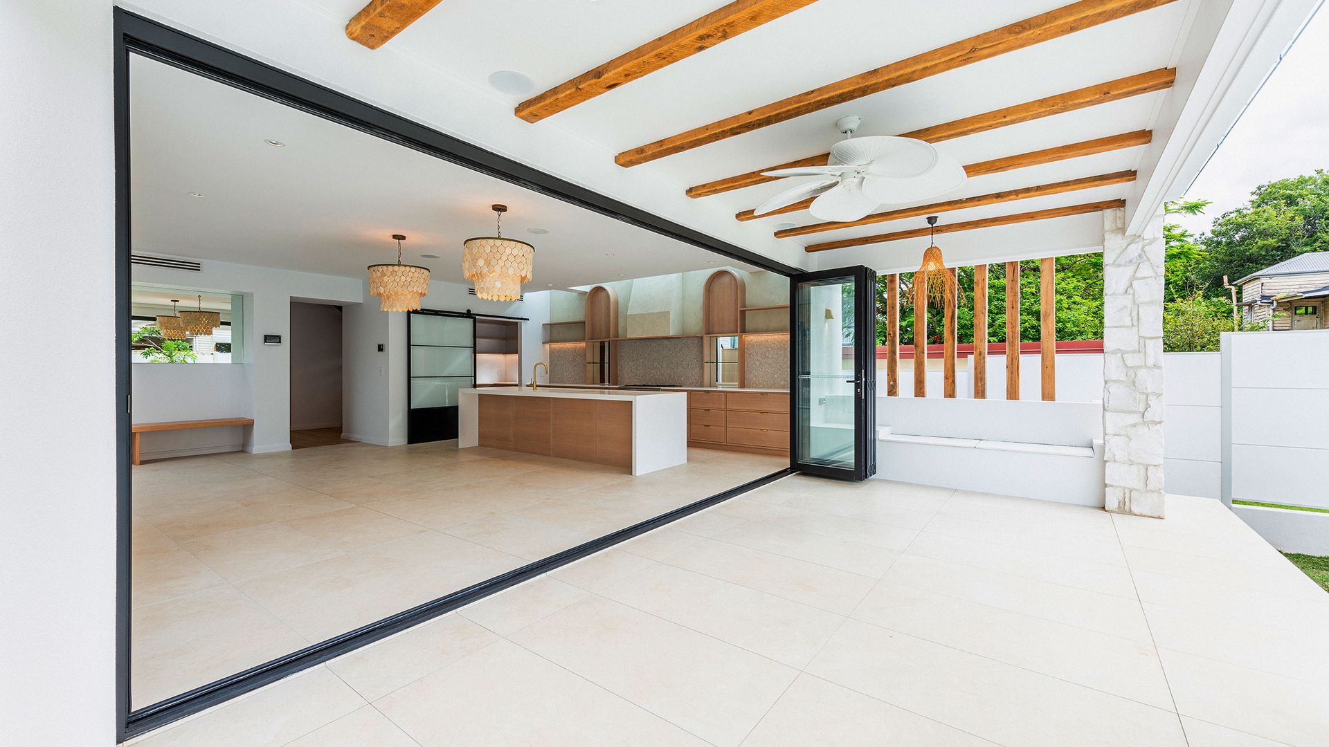 Open indoor/outdoor kitchen with wooden ceiling beams and sliding glass doors; light wood tones, beige floors — K & J Glass in Valla Beach, NSW