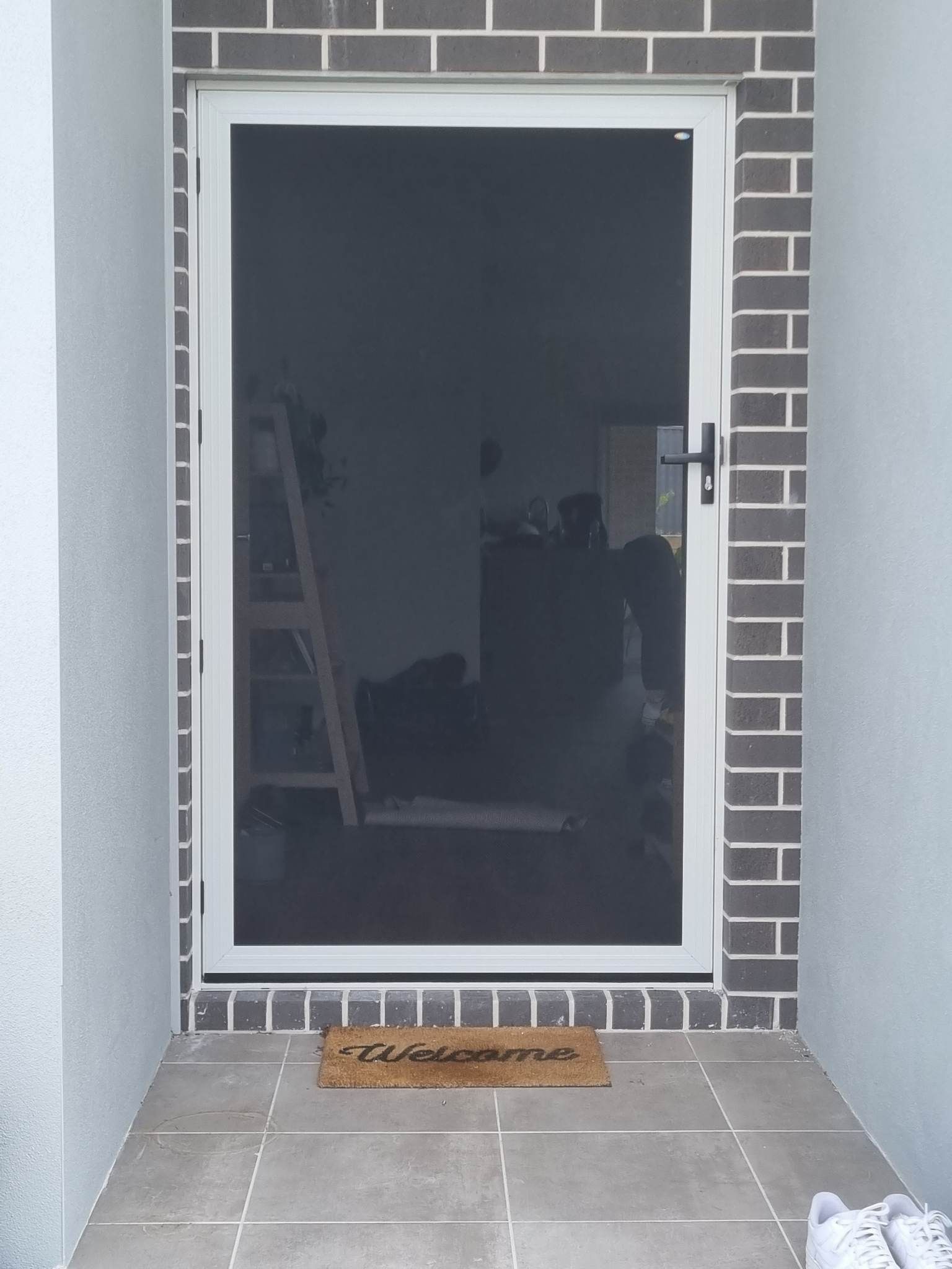 Exterior view of a white-framed screen door, set in a brick facade,