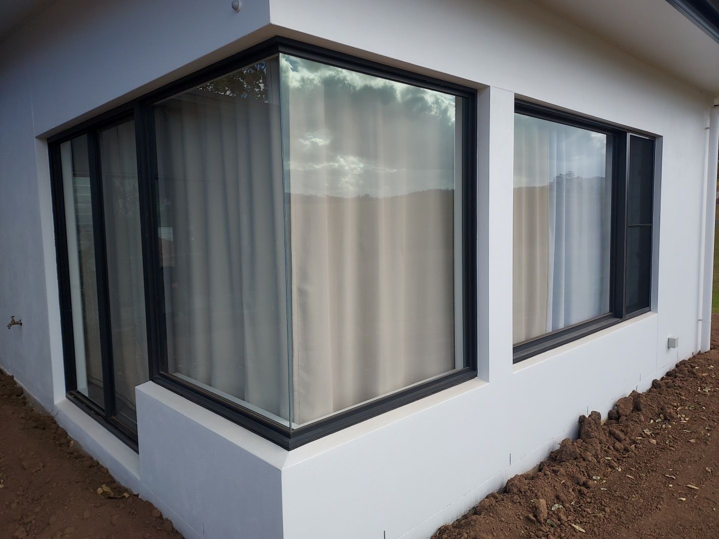 Corner Windows on a White Building, Framed in Black, With Beige Curtains — K & J Glass in Warrell Creek, NSW