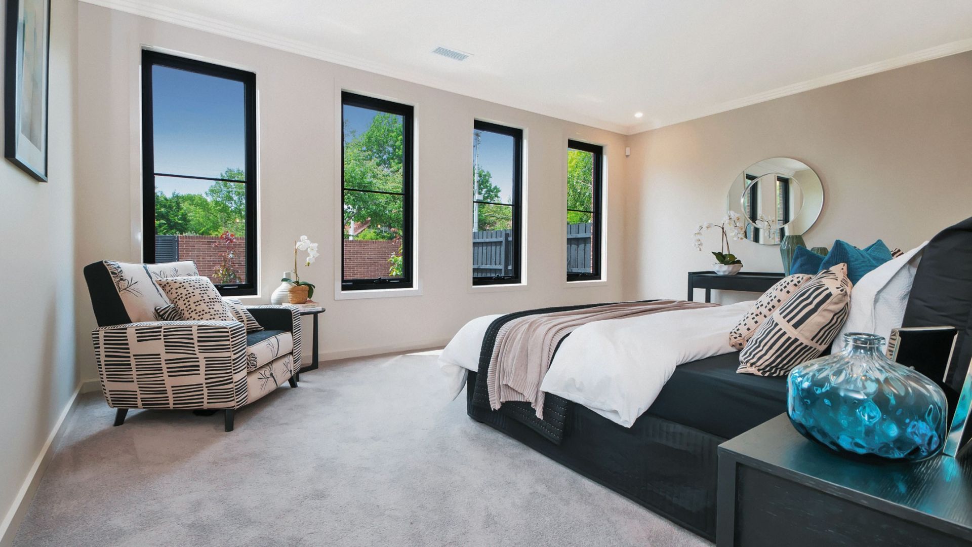 Bedroom with black-framed windows, bed, armchair, and side table with decorative elements — K & J Glass in Scotts Head, NSW