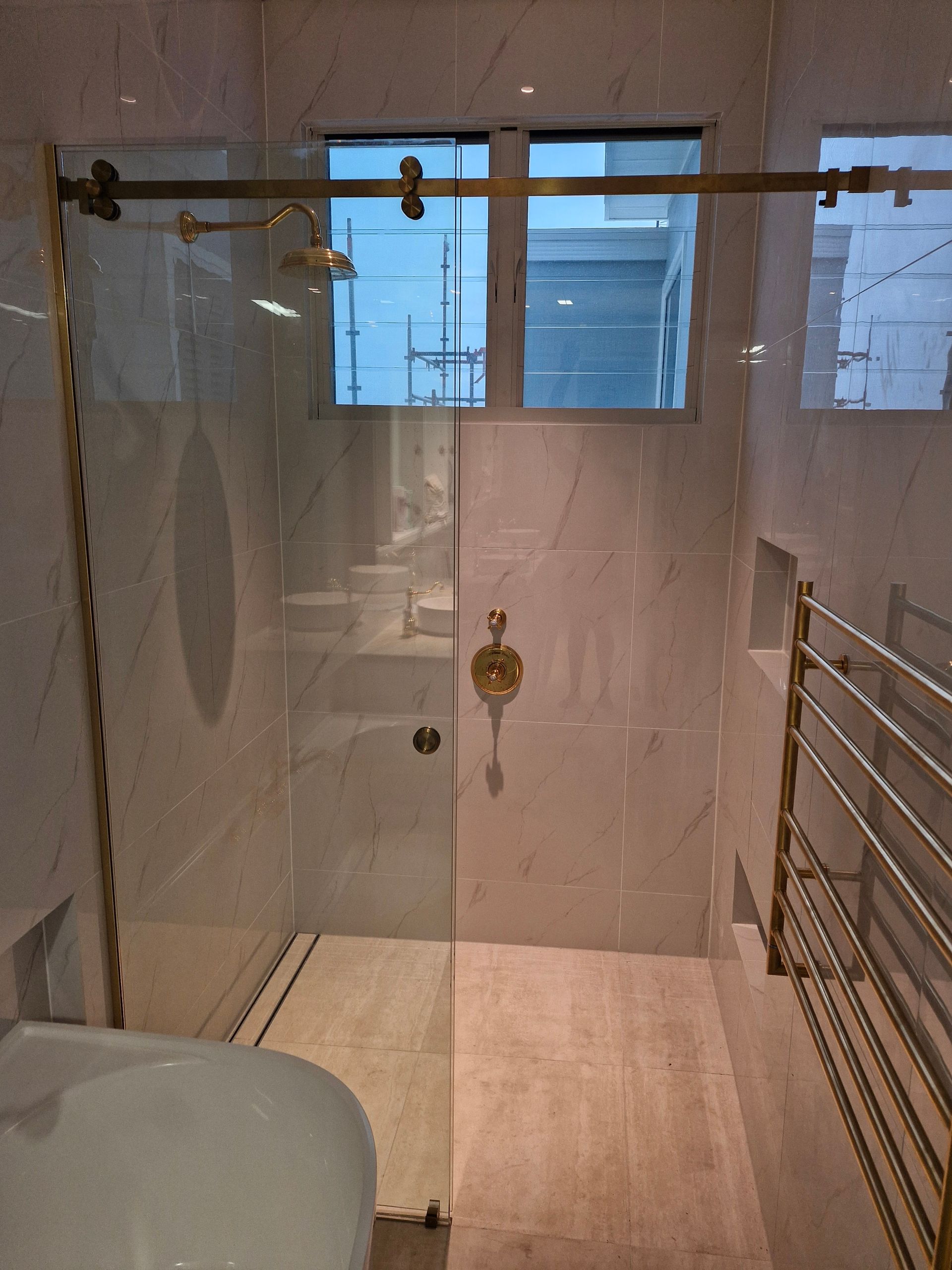 Elegant bathroom with gold accents, glass shower door, and marble tile — K & J Glass in Scotts Head, NSW
