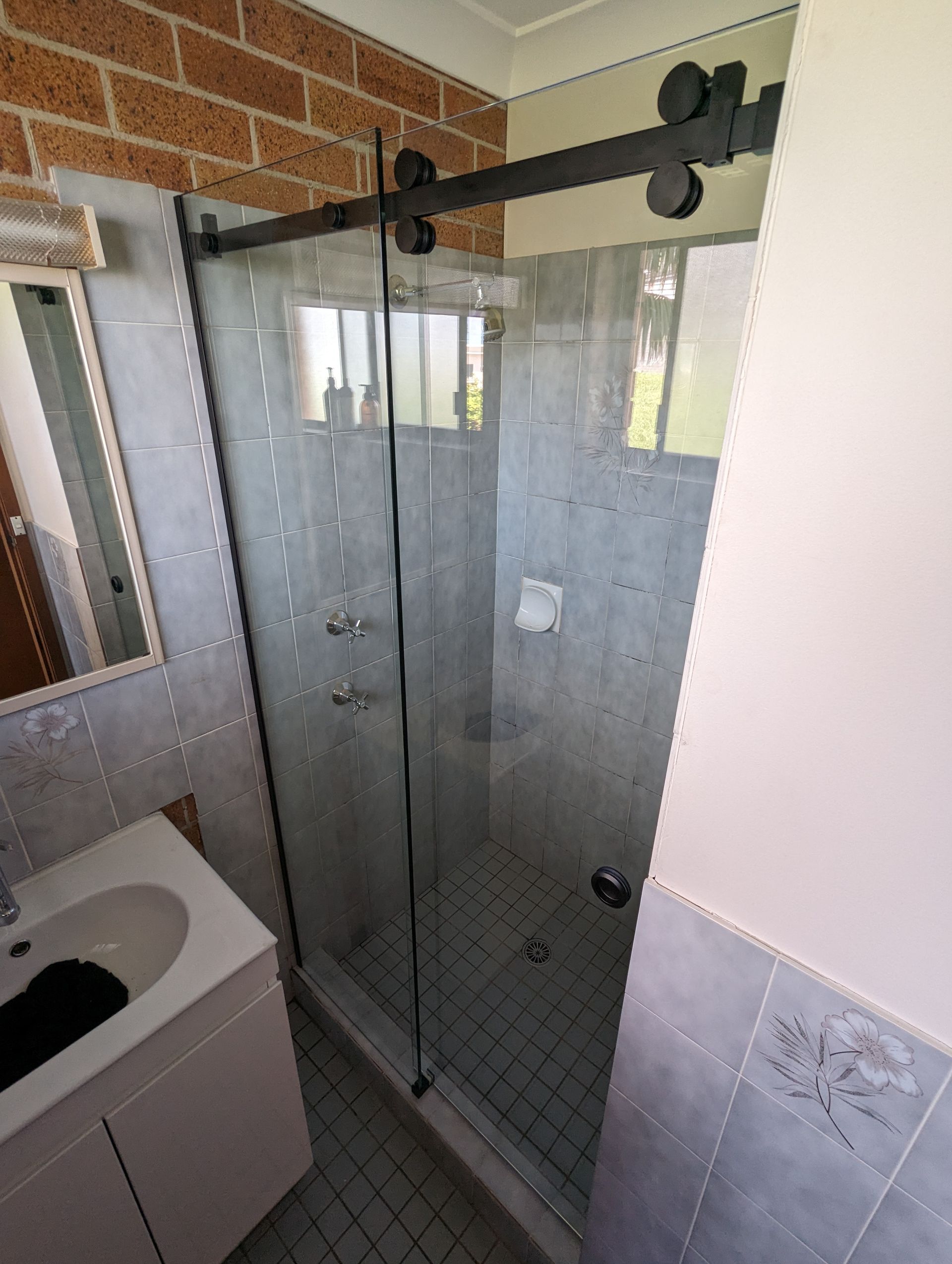 A large sliding shower door with black metal accessories — K & J Glass in Warrell Creek, NSW