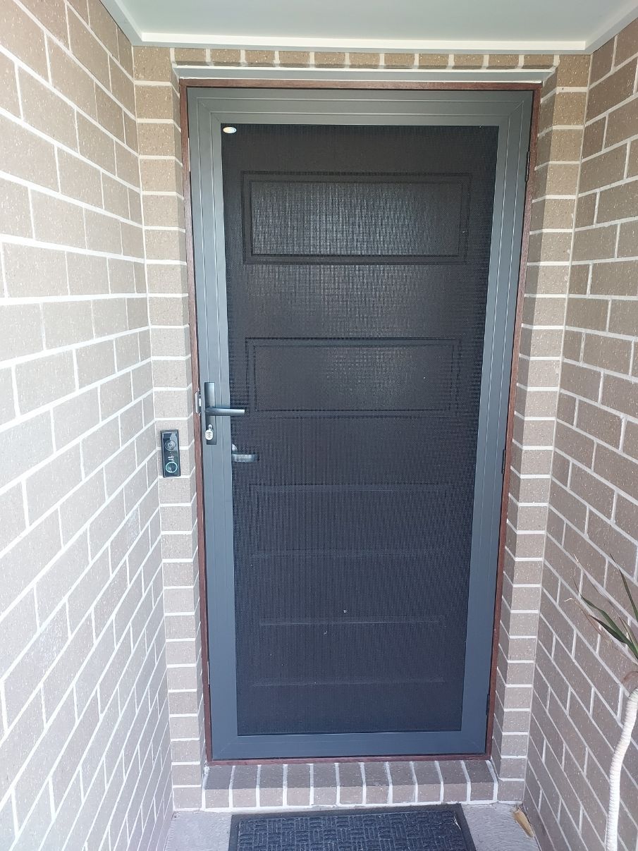 Screen door with dark mesh, set in a brick doorway. Silver frame, handle and lock — K & J Glass in Bowraville, NSW