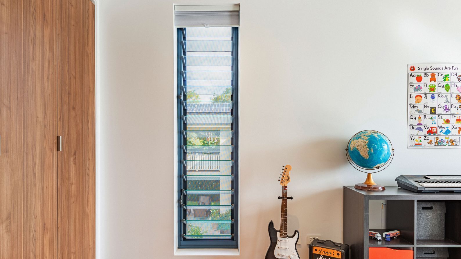 A glass louvre window in a room with brown wooden cupboards and a guitar— K & J Glass in Warrell Creek, NSW