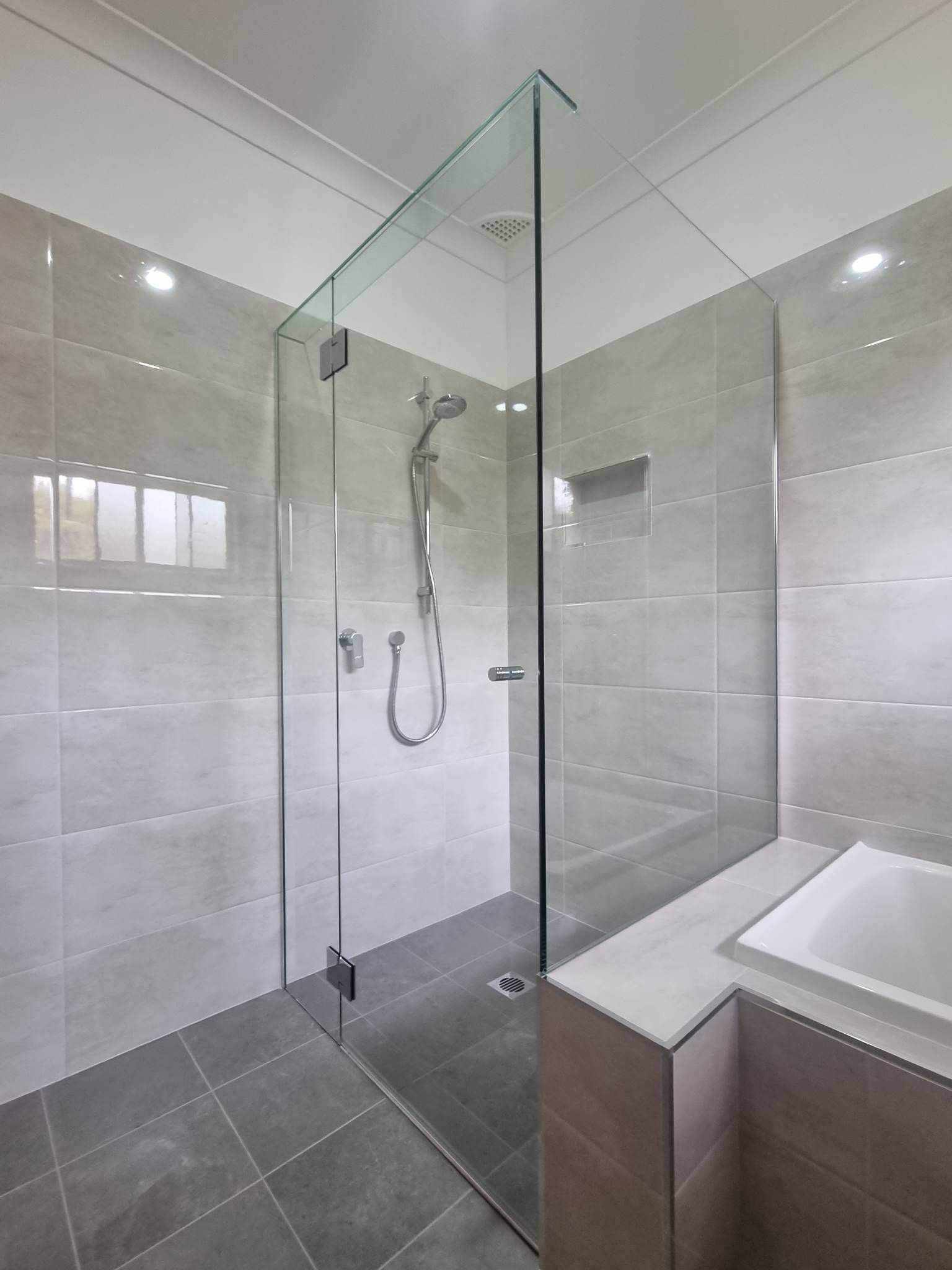 Glass shower enclosure in a modern bathroom with grey tiles — K & J Glass in Warrell Creek, NSW