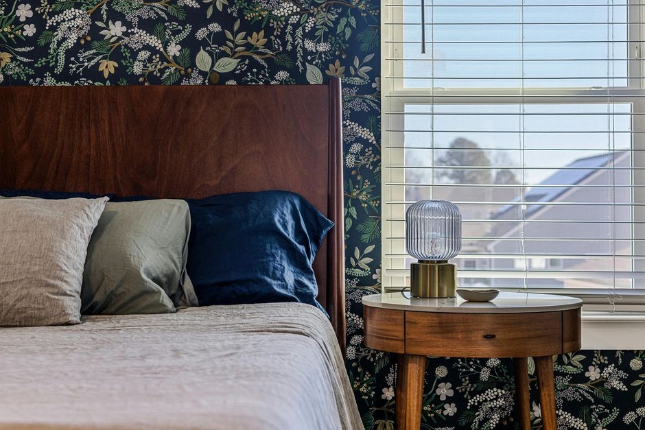 A bedroom with a bed , nightstand and window with blinds.