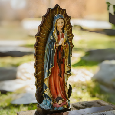 Statue of Our Lady of Guadalupe, blue and red robes, dove, halo, outdoor setting.