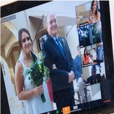 Bride walks with her father during a virtual wedding. Zoom meeting shows other guests watching.