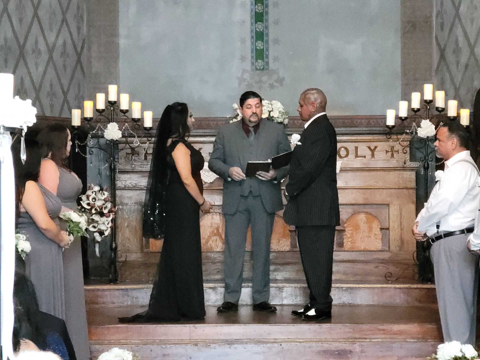 Couple dressed in black stand with Rev. Steve during their wedding ceremony at the Flur de Lis Chapel in Upland, CA