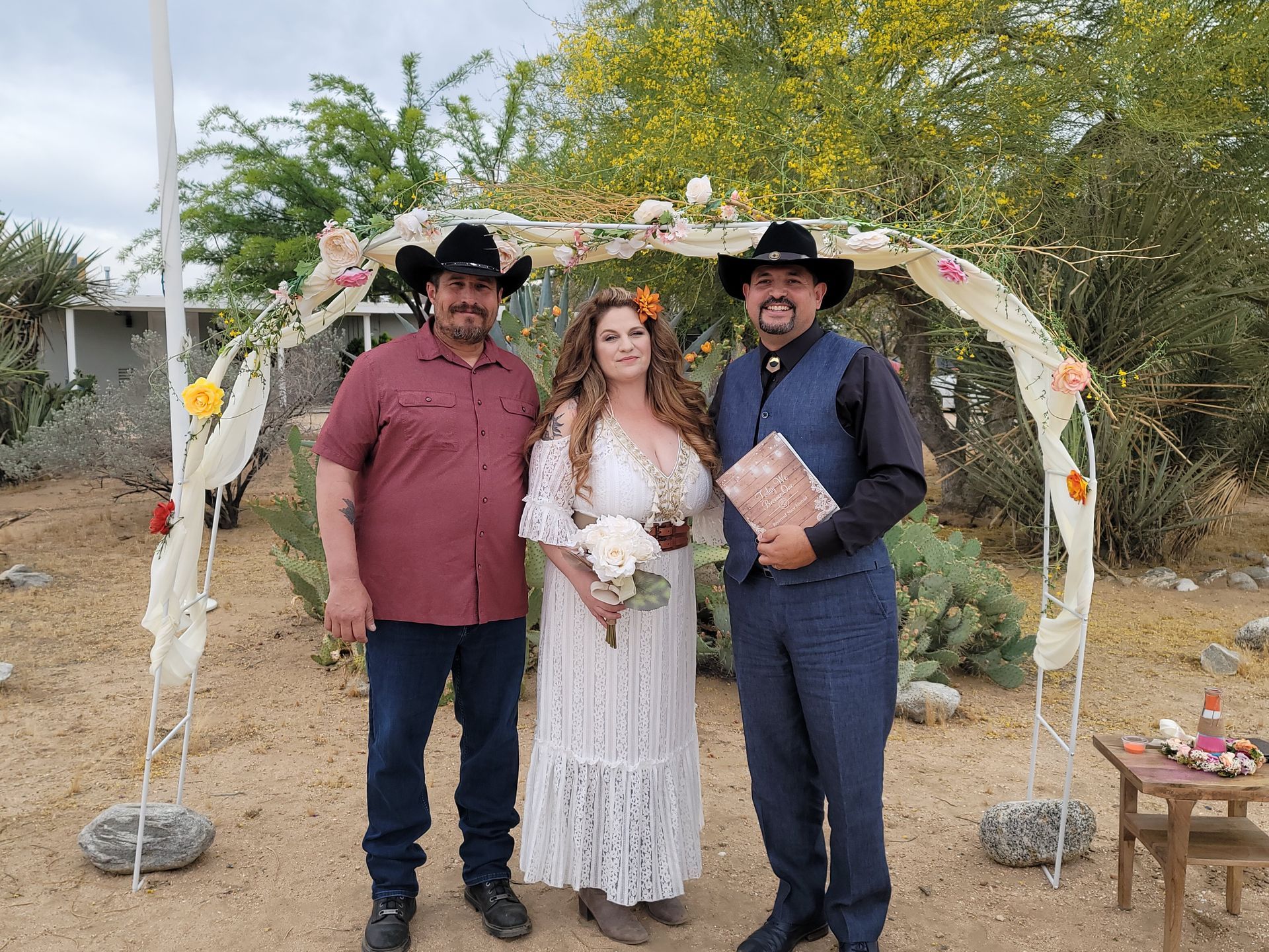 Bride and groom with officiant under floral archway in outdoor wedding.