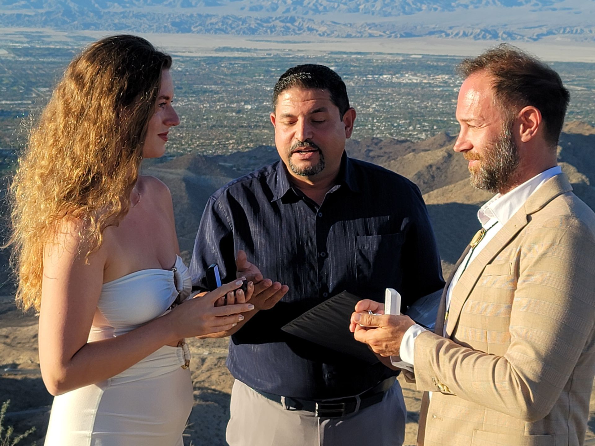 Couple getting married outdoors with officiant, desert landscape background.