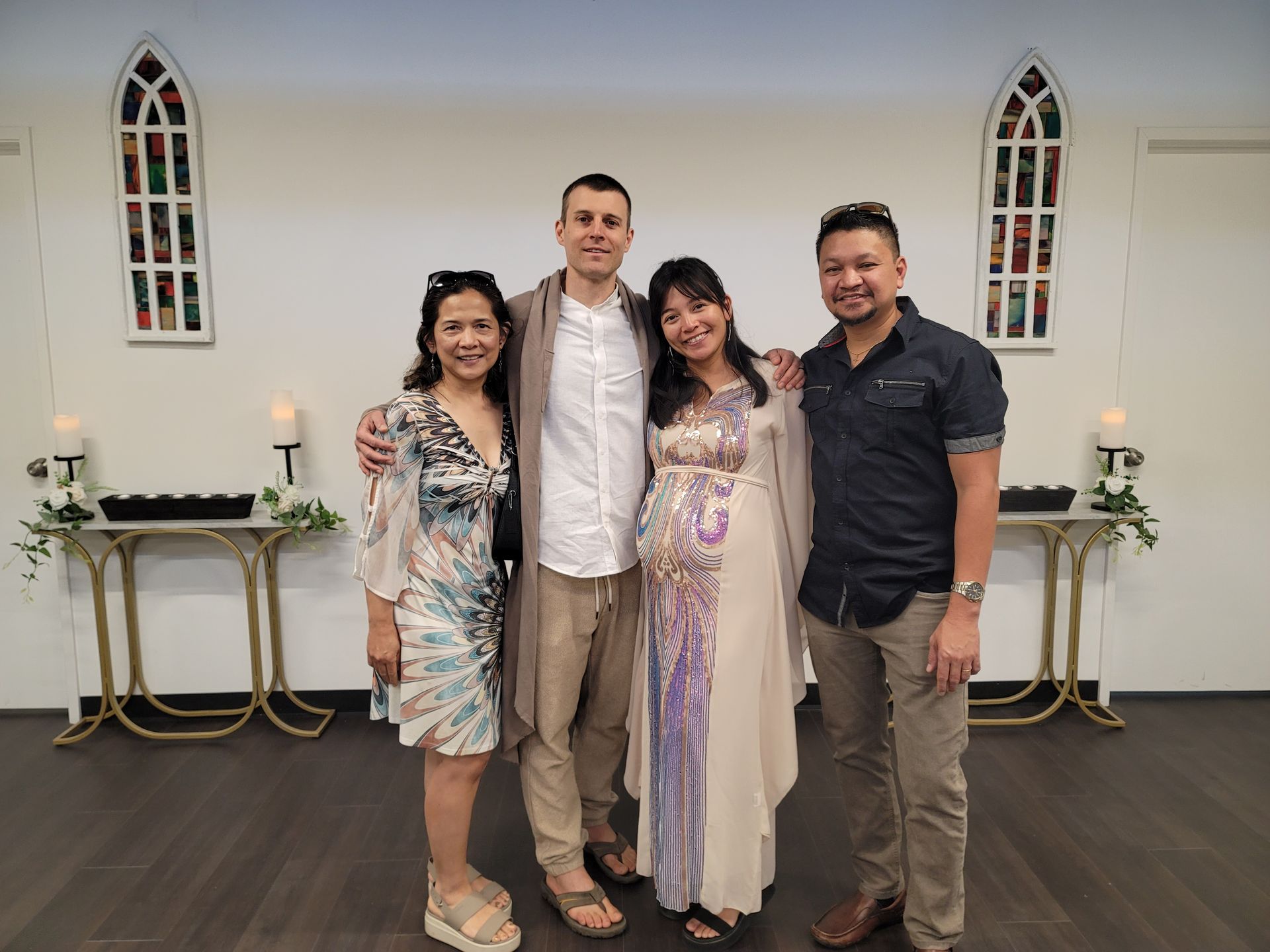 Four people smiling, posing together indoors. Two women and two men in a white room, with white and gold accents.