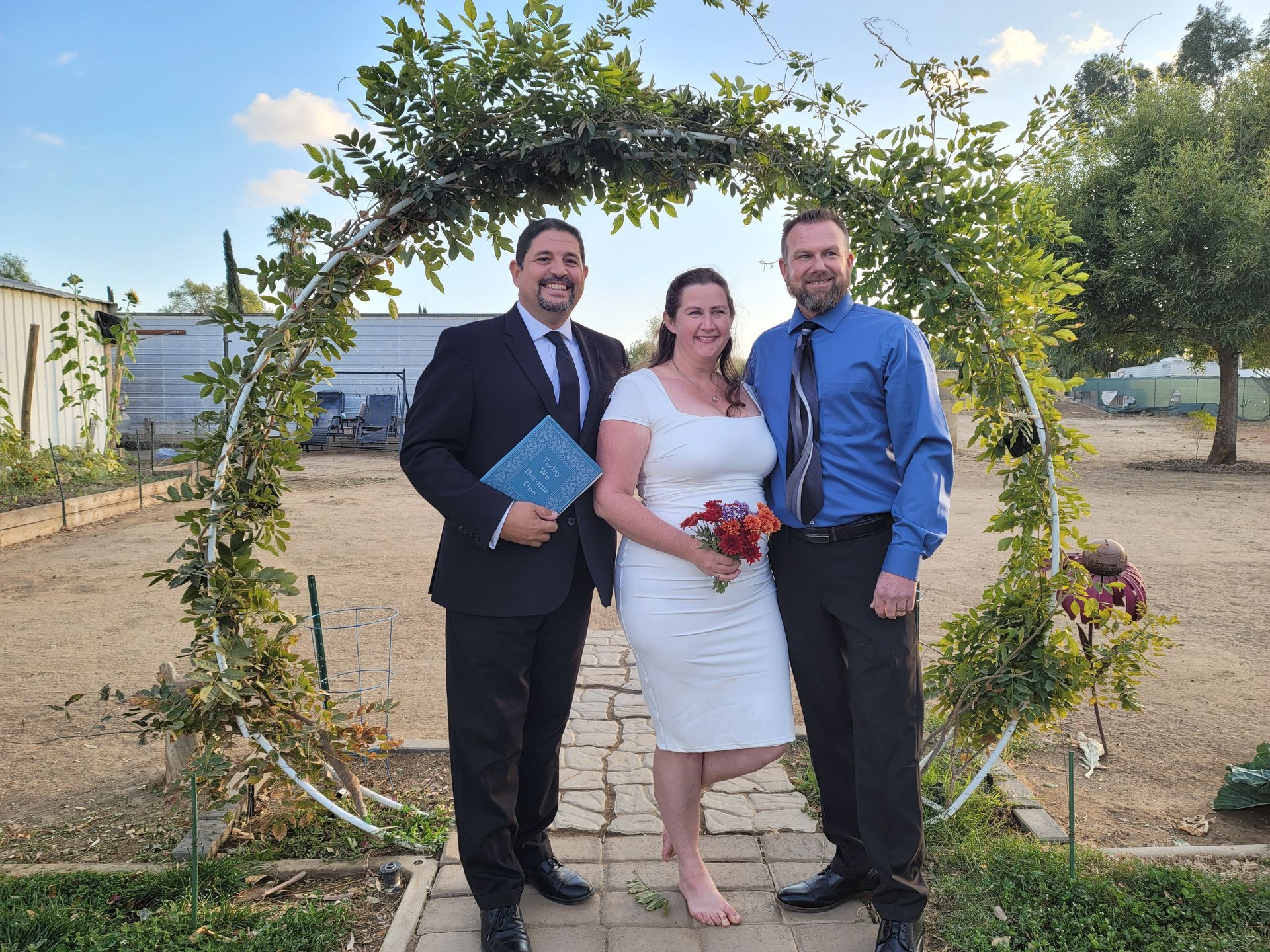 A wedding ceremony with a couple and officiant under a floral arch outdoors.