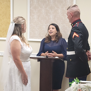 Bride and groom at a wedding ceremony with an officiant; indoors. The groom wears a Marine uniform.