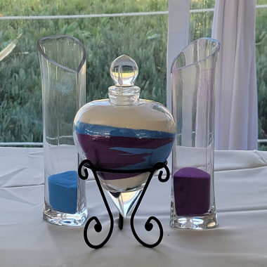 Sand ceremony set with blue, purple, and white sand in clear glass vases, on a white tablecloth.