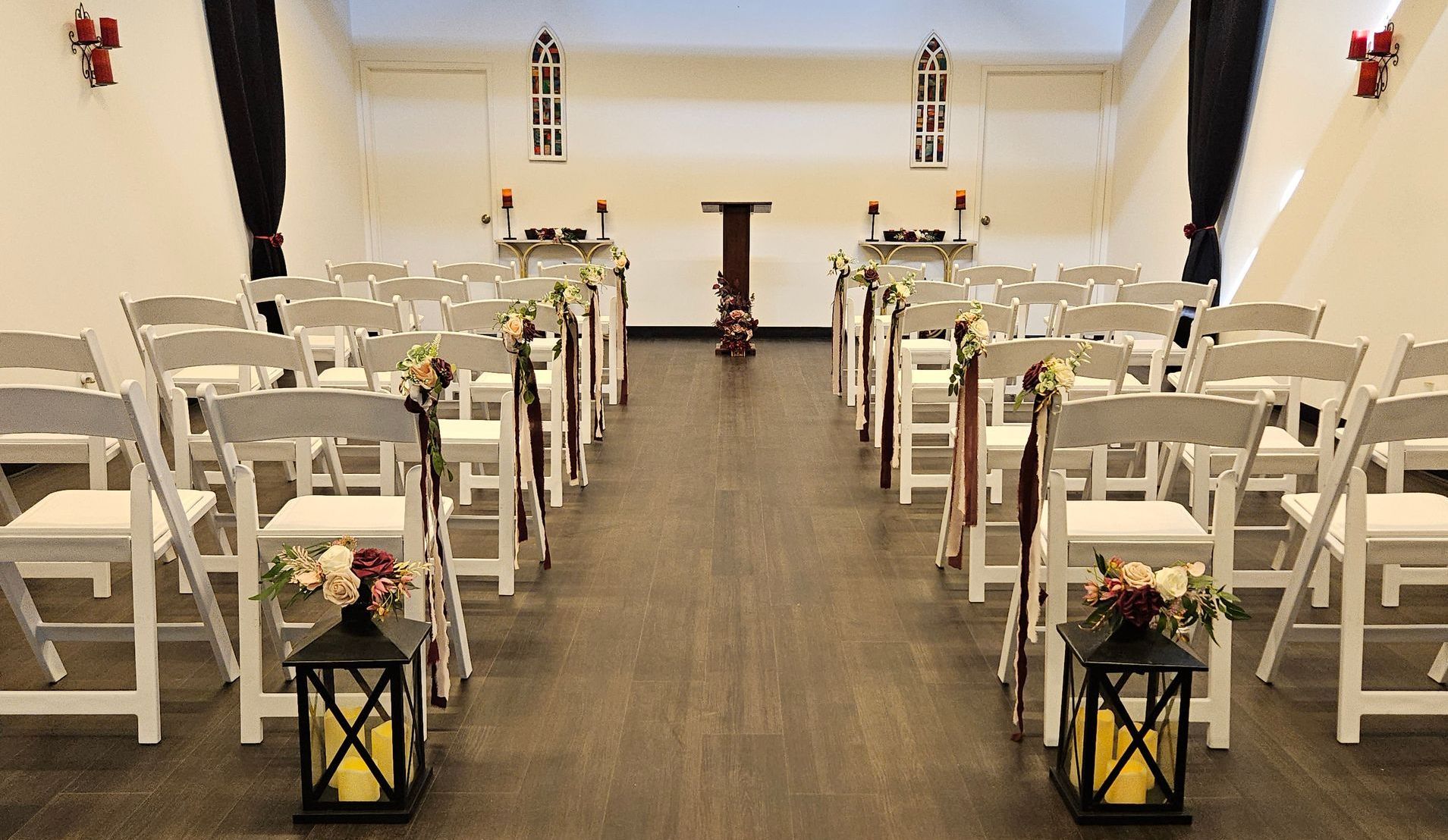 Empty wedding chapel with white chairs, dark floor, and decorations.