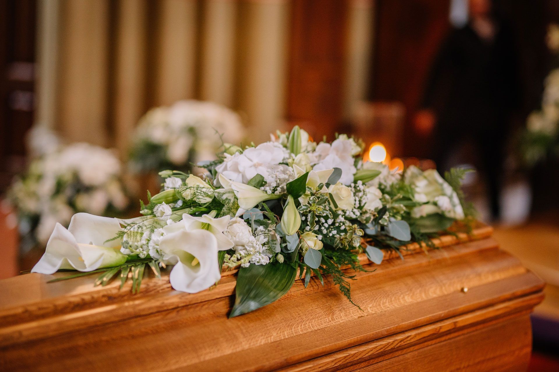 A wooden casket adorned with white flowers in a dimly lit room, likely a funeral.
