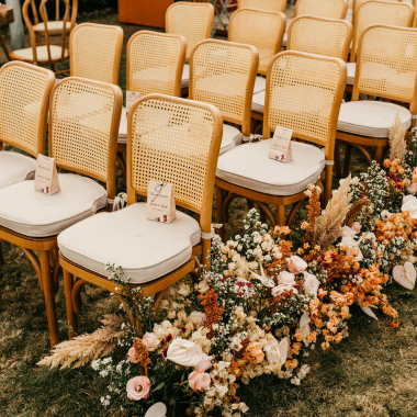 Rows of rattan chairs with floral decorations for an outdoor event.