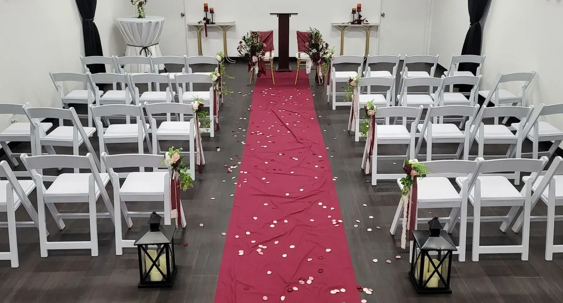 Wedding ceremony setup: white chairs, red aisle runner, floral decorations, and lanterns.