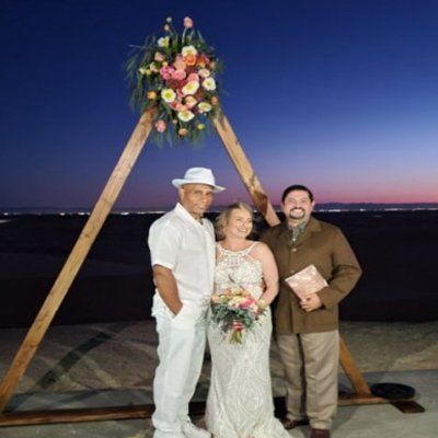 Couple Stands with Rev. Steve with a A-frame Arch as the sun sets at the Glamis Sand Dunes
